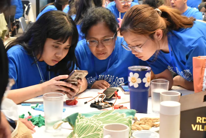Three teachers leaning in over a phone running the control app
