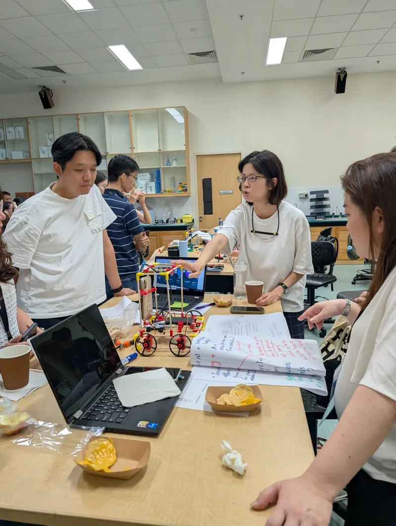 Teachers around a lab bench with a buggy, a laptop and their hand-written plans